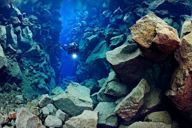 A diver with a torch among huge lava boulders in blue water