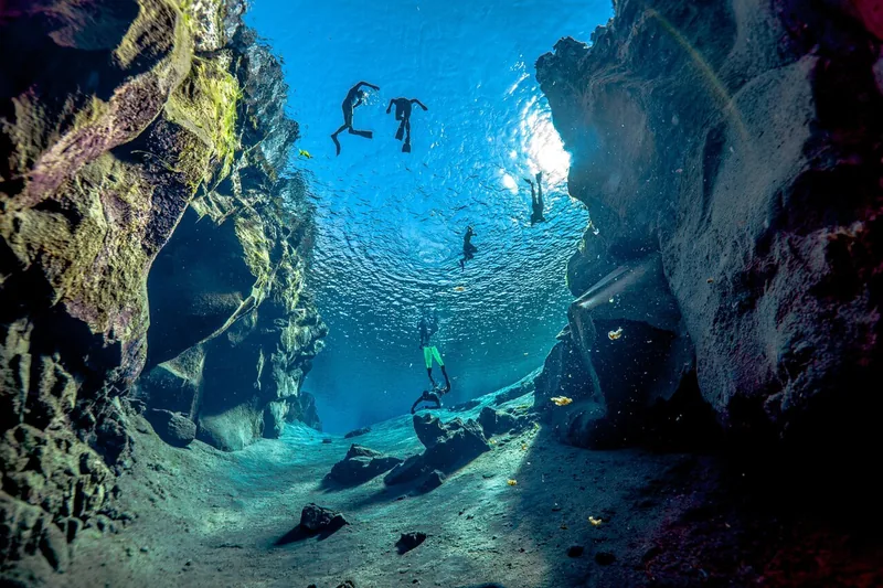 Snorkelers seen from below floating at the surface between tall lava walls
