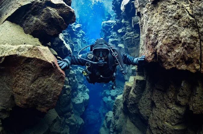 A scuba diver in a drysuit squeezing between two lava boulders