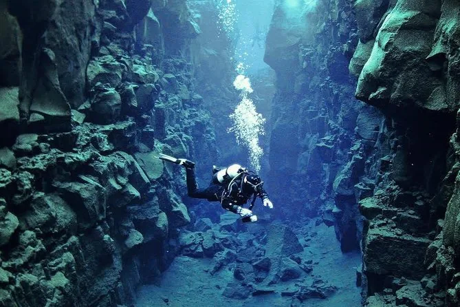 A scuba diver in a drysuit exhaling bubbles between tall lava walls