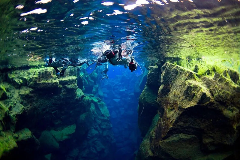 A small group of snorkelers floating above a deep green and blue crack