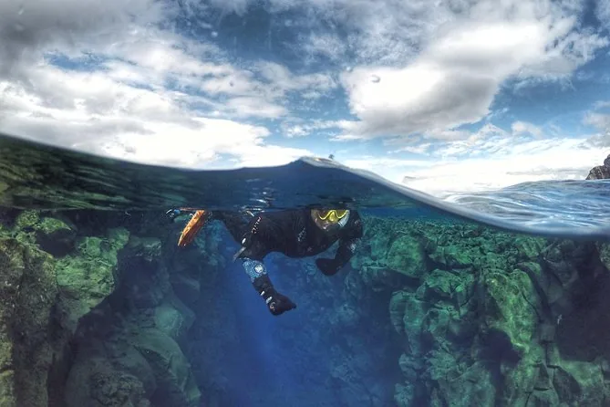 A snorkeler in a drysuit and yellow fins, half above and half below the water line
