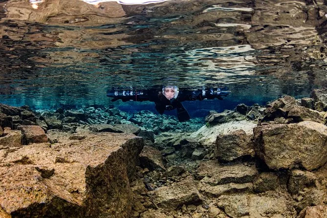 A snorkeler in a drysuit gliding over shallow lava boulders