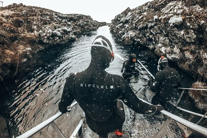 A snorkeler in a thick wetsuit and hood walking down the metal entry steps into the fissure